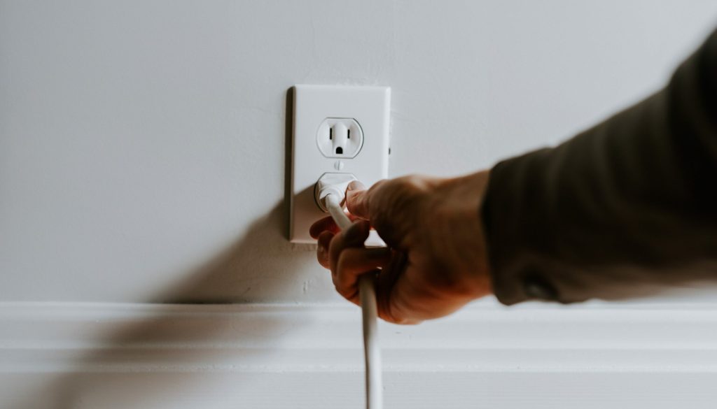 A person removing a plug from a wall outlet