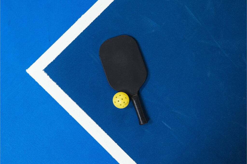 Pickleball paddle and ball resting on the edge of a court