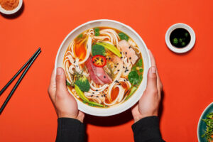 Bowl of ramen on a red table with chopsticks and sauce