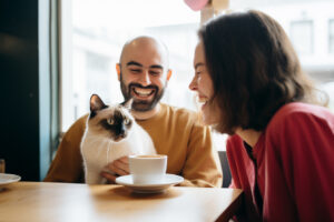Couple with cat drinking a catpuccino sitting and laughing at a table
