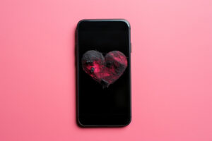 A black phone with a pink and black heart on its screen against a pink background