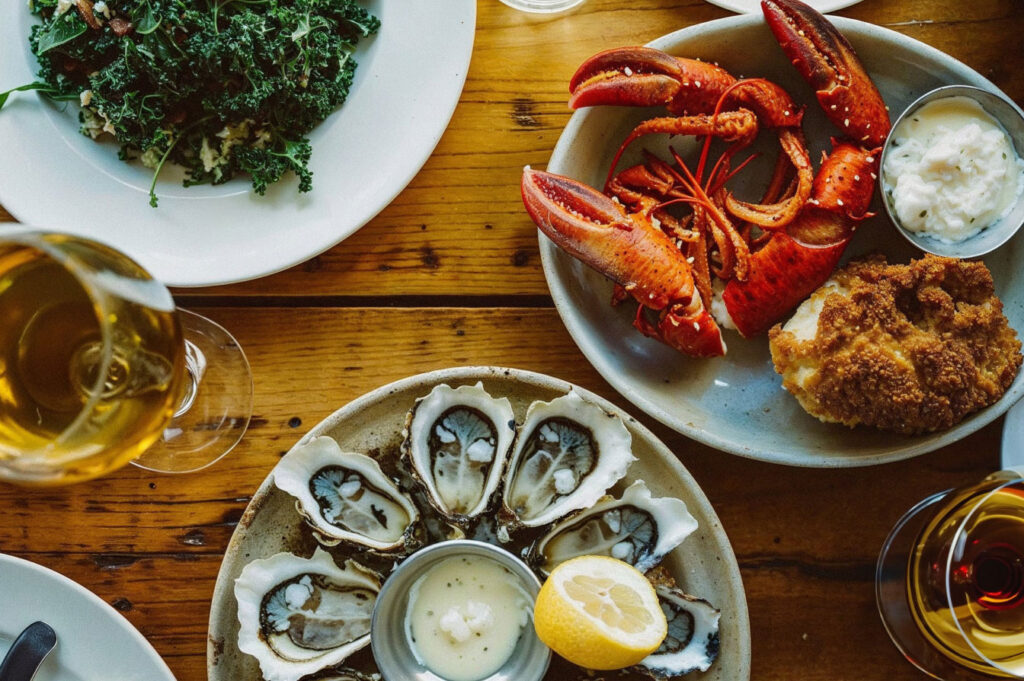 Wooden Table Adorned with Plates of Seafood, a Kale Salad, and Wine Glasses
