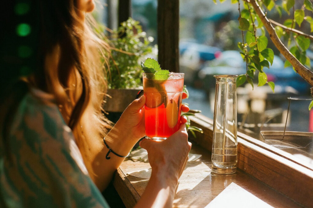 Person enjoying a cocktail by a sunny window.